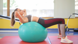Mulher faz exercício de pilates no solo com bola suíça para fortalecer o abdômen e melhorar a postura.