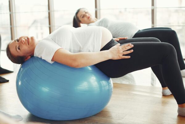 Gestante faz exercício com bola de pilates durante aula de atividade física para gravidez.