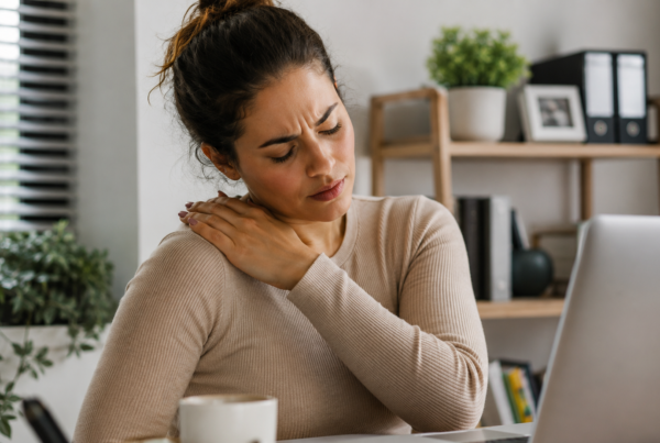 Mulher em ambiente de trabalho massageia o ombro enquanto sente tensão muscular causada pelo estresse e pela sobrecarga da rotina.