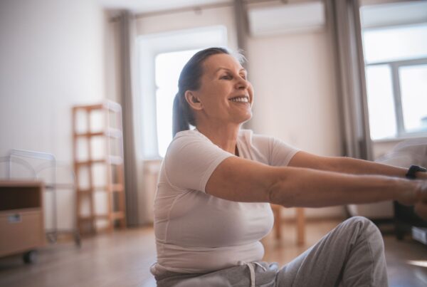Mulher madura sorrindo enquanto pratica exercícios físicos em ambiente interno iluminado, promovendo saúde e bem-estar durante a menopausa.