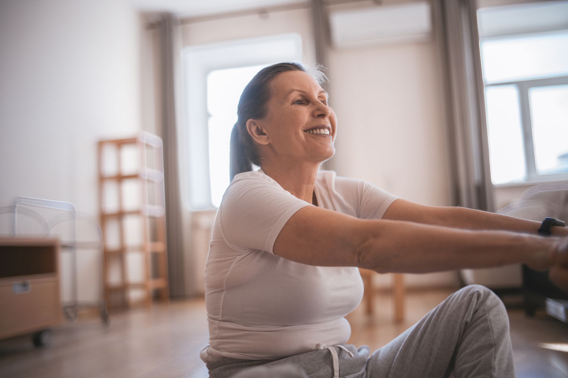Mulher madura sorrindo enquanto pratica exercícios físicos em ambiente interno iluminado, promovendo saúde e bem-estar durante a menopausa.