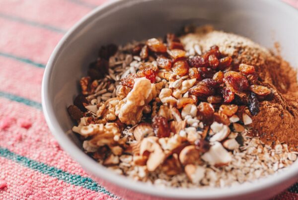 Tigela com aveia, sementes, castanhas, uvas-passas e canela, ilustrando uma refeição rica em fibras e nutrientes para uma alimentação saudável.