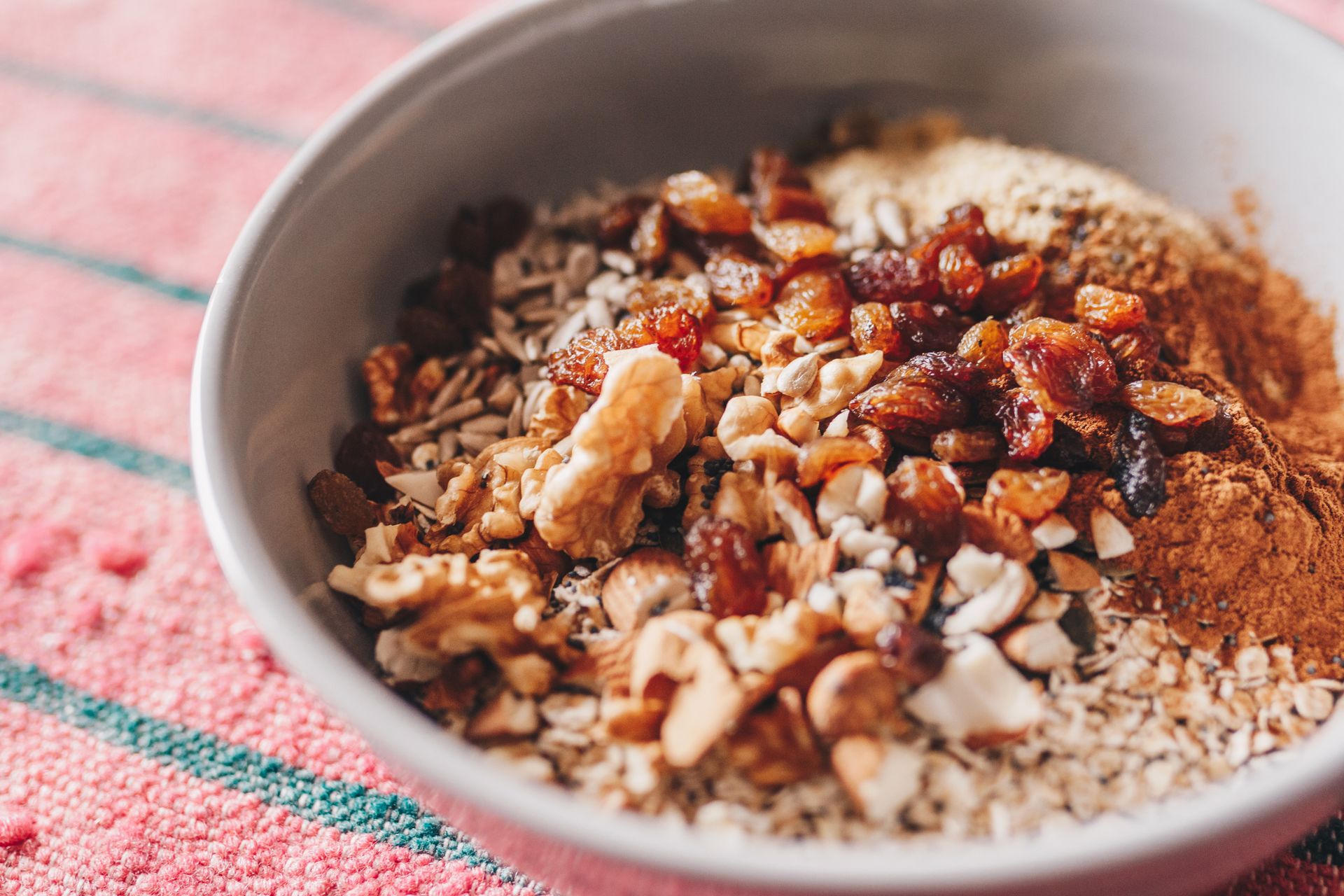 Tigela com aveia, sementes, castanhas, uvas-passas e canela, ilustrando uma refeição rica em fibras e nutrientes para uma alimentação saudável.